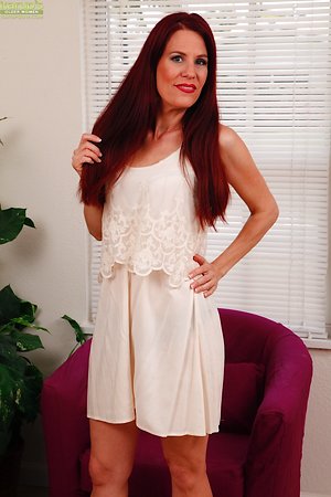 Auburn-haired mature puts fingers into pussy in armchair